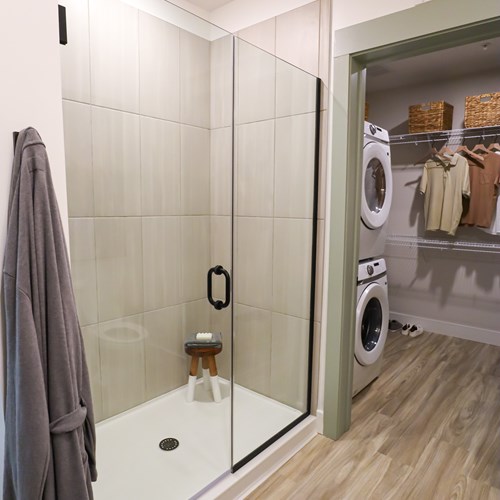 glass framed shower with view into unit closet with stacked washer and dryer